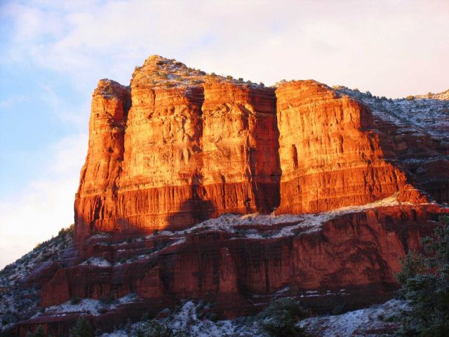 Late afternoon sun illuminates a red rock mesa with a dusting of snow. Picture