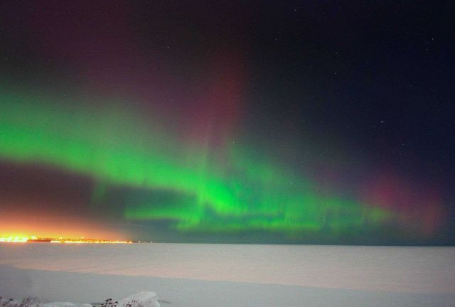 Northern lights dancing over a frozen Lake Superior while the lights of Marquette twinkle in the distance Picture