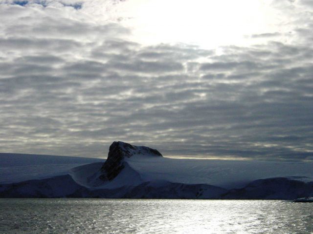 An angular mountain peak looking like the prow of a ship seemingly cuts through an Antarctic Peninsula ice field. Picture
