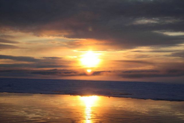 Sun, reflections off new ice, clouds, pack ice, and new ice forming at the edge of the pack ice. Picture