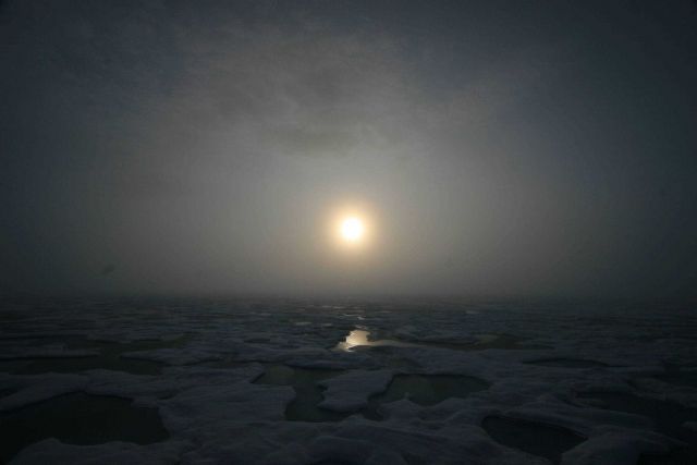 Sun seen through the clouds over melt pools and hummocky ice on a gloomy day. Picture