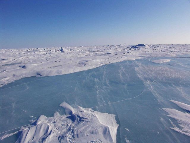 Looking over a frozen melt pond towards a hummocky ice landscape in multi-year ice. Picture