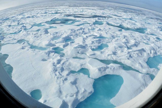 Looking through a porthole of the HEALY to view of second or multi-year ice with aquamarine melt pools . Picture