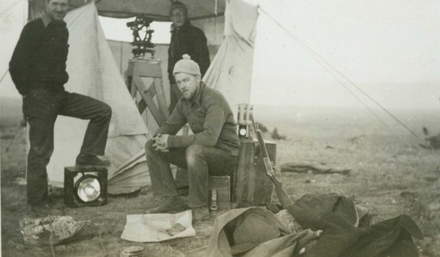 Bill Husemeyer at the theodolite and Vic Smith sitting on instrument bow at a station along the 46th Parallel in Montana. Picture