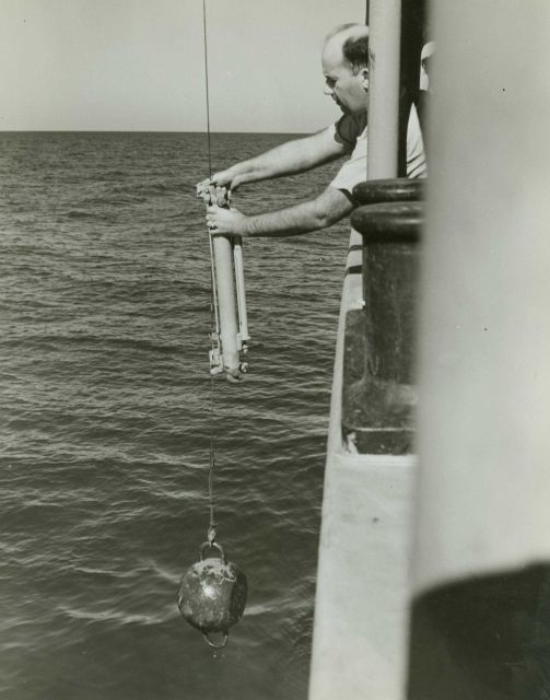 Commander Marvin Paulson hanging a Nansen bottle for collecting water specimen and measuring temperature at depth. Picture