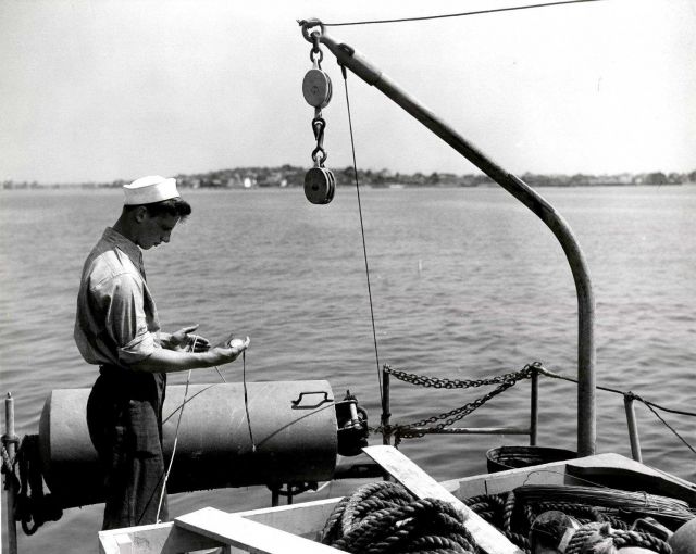 Current pole measurements by seaman using stop watch to determine velocity of current as pole carries out line. Picture