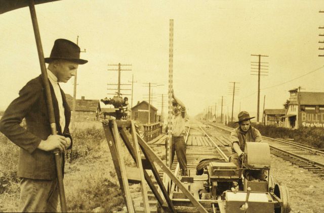 Recorder sitting while working with tabulating machine; umbrella man shading leveling instrument; and rodman holding rod vertical over turning point Picture