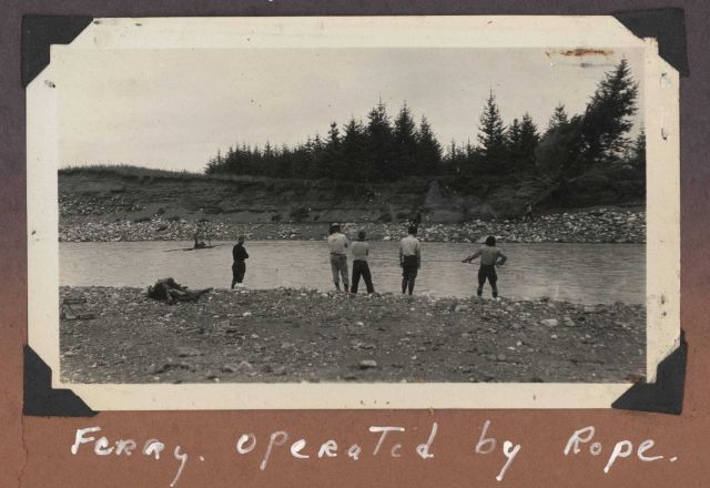 Work party crossing stream on improvised ferry operated by rope. Picture