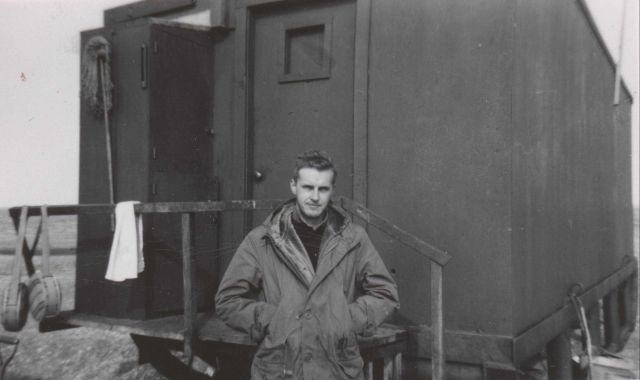 Lt.(j.g.) Harley Nygren outside a wanigan, a portable sled mounted shelter. Picture