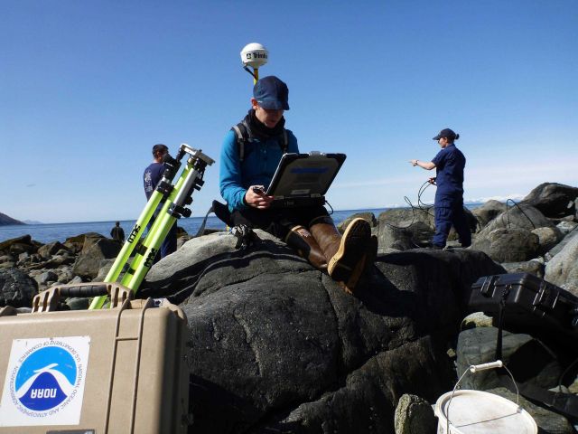 Senior Survey Technician Brandy Geiger with Trimble satellite positioning system determining location of tide gage site as other members of work crew  Picture