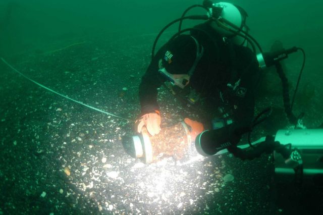 Steve Sellers, Diving Safety Officer of East Carolina University, holding measuring tape to map location of Kad'yak's hub prior to recovery for preser Picture
