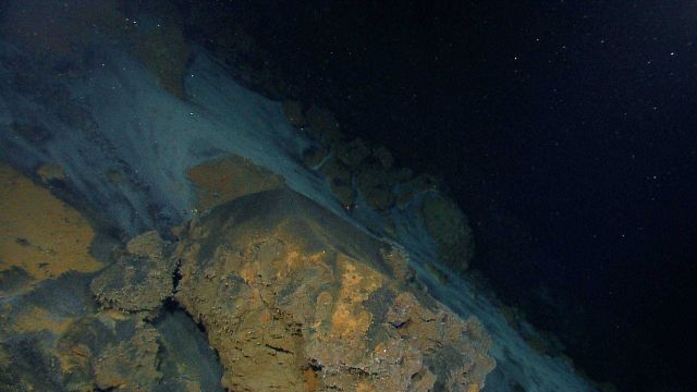 A kaleidoscopic landscape of black, orange, and white colors composed of hydrothermally altered rocks and sediments and bacterial mat material. Picture