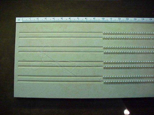 The slotted board used for stringing cultured pearls and measuring the length of the necklace or bracelet. Picture