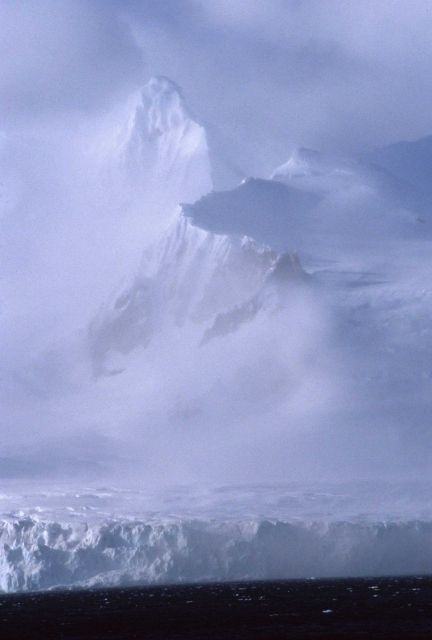 Snow-shrouded mountain peaks rising seen through storm clouds Picture