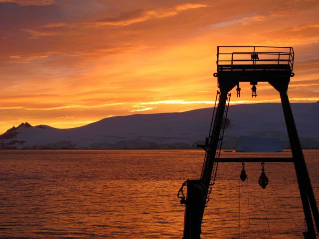 The sun rises over the R/V Moana Wave in Discovery Bay, Antarctica. Picture
