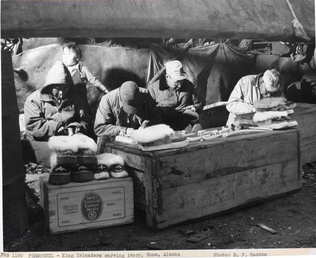 King Islanders carving ivory beneath the skin-covered umiaks on the beach at Nome where they have a summer camp. Picture