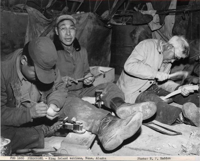 King Islanders carving ivory beneath the skin-covered umiaks on the beach at Nome where they have a summer camp. Picture
