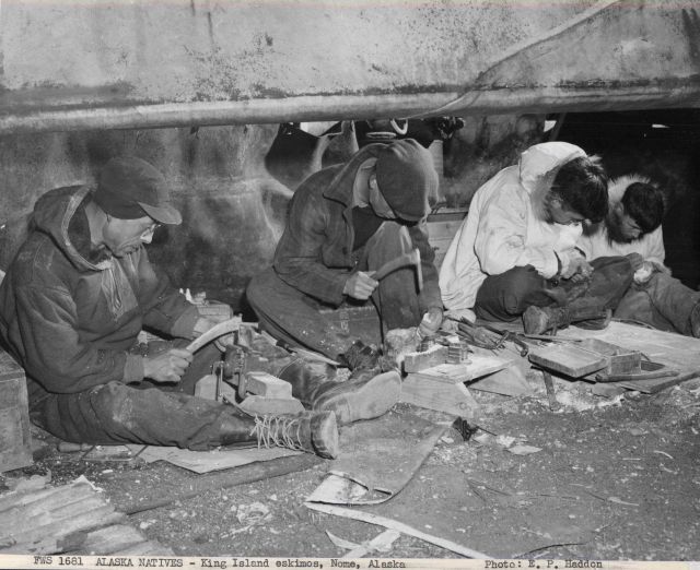 King Islanders carving ivory beneath the skin-covered umiaks on the beach at Nome where they have a summer camp. Picture