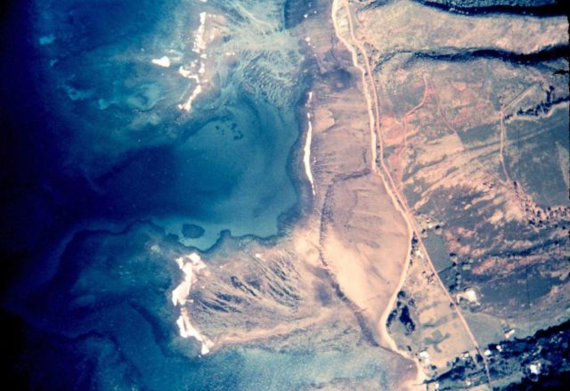 Aerial photograph of tropical island shoreline showing reefs and other underwater features. Picture