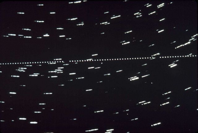 Typical photograph plate showing stars in circular pattern and satellite image showing as series of dots in straight line. Picture