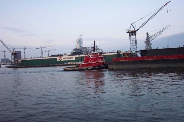 Tug pushing barge down the Elizabeth River with Navy ship in drydock. Picture