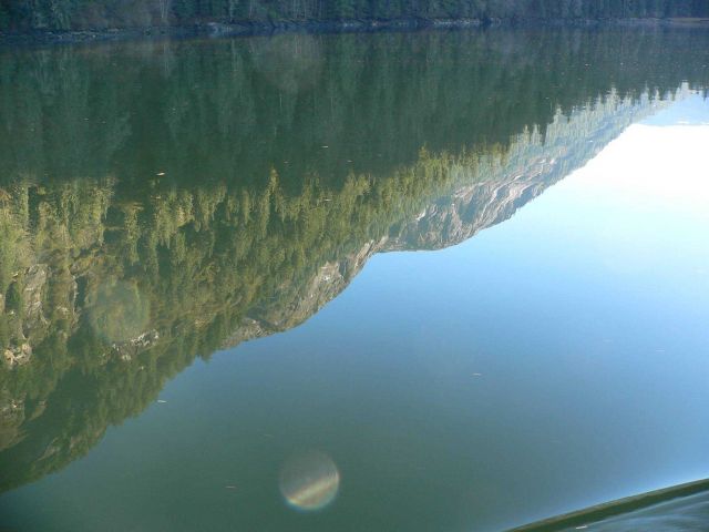 A mirror-like reflection of mountains and trees on a placid inlet. Picture