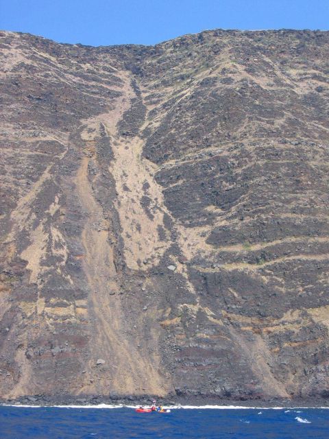 A Safeboat from the NOAA Ship OSCAR SETTE is dwarfed by multiple lava flows forming a cliff on the coast of Hawaii Picture