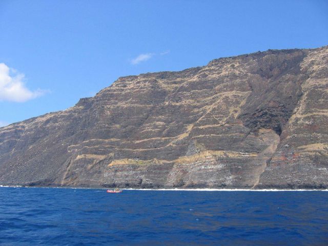 A Safeboat from the NOAA Ship OSCAR SETTE is dwarfed by multiple lava flows forming a cliff on the coast of Hawaii Picture