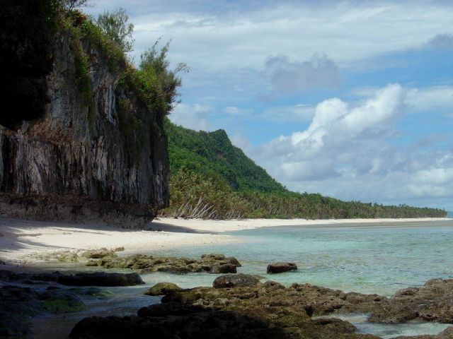 Eroding coral rock, wave undercut cliffs, pristine beach, palm trees, and jungle on Guam. Picture