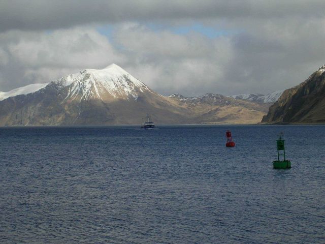 A volcanic cone, buoys, and a fishing vessel complete a Dutch Harbor scene. Picture