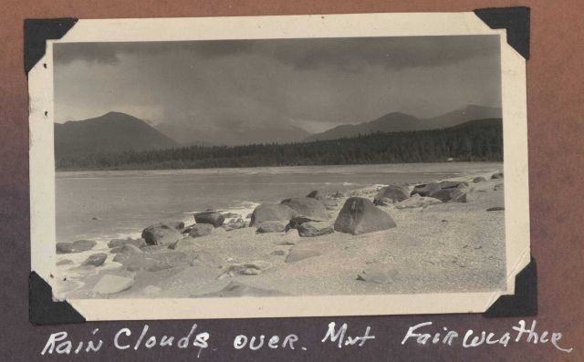 Looking over a sand and boulder beach to Mount Fairweather enveloped in rain clouds. Picture
