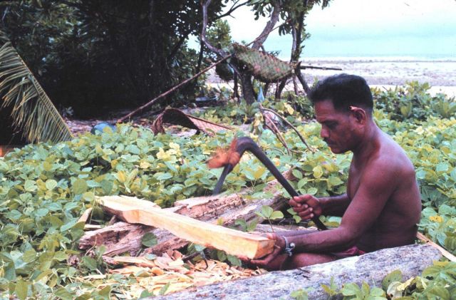 Native Micronesian making a paddle with an adze for his outrigger canoe. Picture