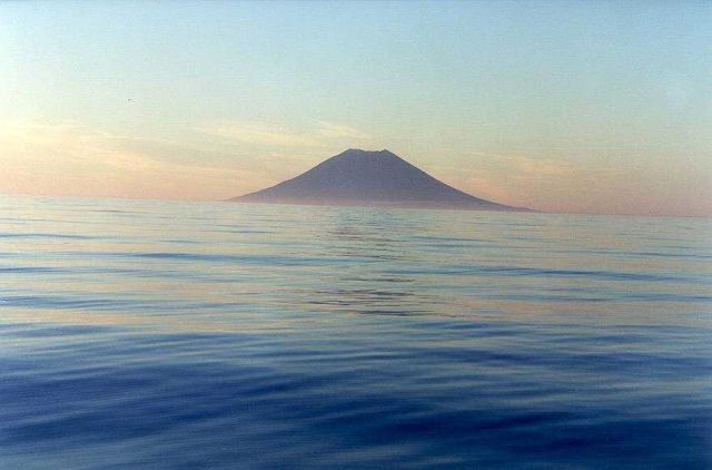 A symmetrical volcanic cone in the Kurile Islands seen at dawn over a calm north Pacific Ocean. Picture