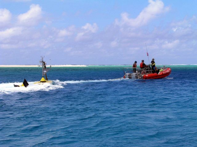 Oceanographers tow a CREWS buoy through a channel for deployment inside an atoll . Picture