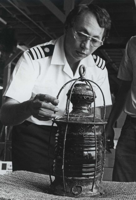 Commander Phil Johnson inspecting lantern recovered from the MONITOR. Picture
