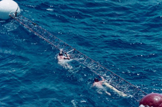 Swimmers assist in guiding solar radiance tower to buoy for mounting and installation. Picture