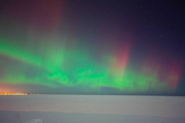 Aurora borealis over a frozen Lake Superior with the lights of Marquette on the shore. Picture