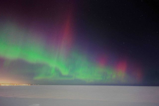 Aurora borealis over a frozen Lake Superior with the lights of Marquette on the shore. Picture