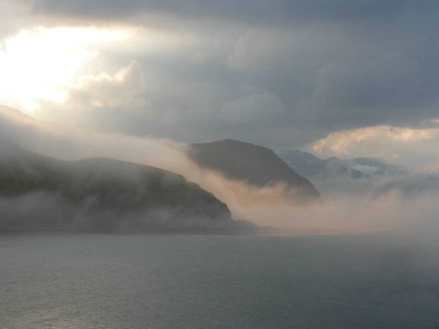 Early morning sun illuminating fog streaming off the mountains of Dutch Harbor. Picture