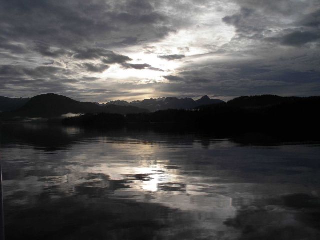 Late afternoon sun shining through the clouds and reflecting on the waters of a placid bay. Picture