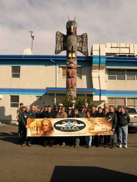 Personnel of the OMAO Marine Operations Center-Pacific proudly display the NOAA 200th Banner outside the headquarters building of the Marine Center Picture