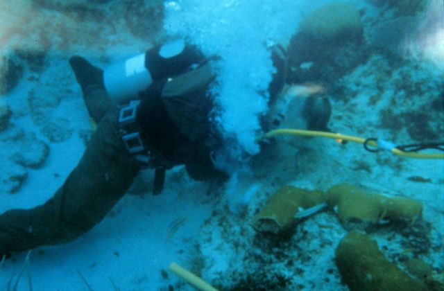 A diver uses a pneumatic drill to create a hole in the reef framework to secure loose coral fragments. Picture