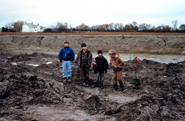 Local children stand in the low marsh area adjacent to the pre-restored ditch of a headwater stream. Picture