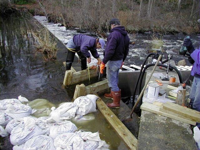 John Catena, of NOAA, supervises the crew as the ladder is being installed and fitted into the cut in the dam. Picture