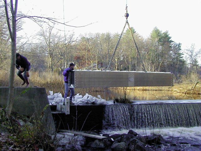 The first section of the fish passway is lowered and guided toward the notched area of the dam where it will be fitted into place and secured. Picture