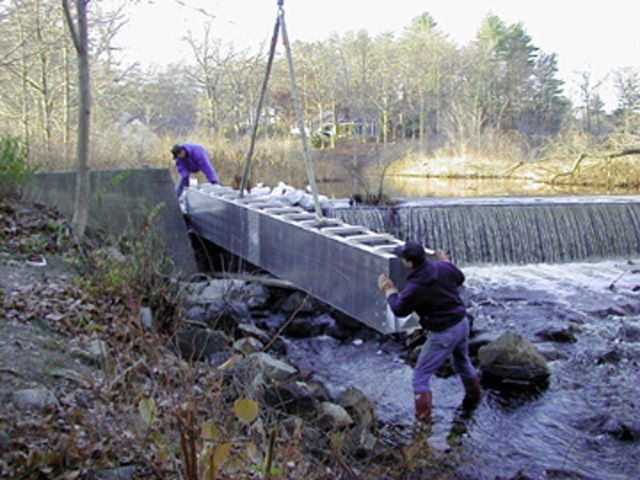 Two workers guide the first section of the fish ladder into place. Picture
