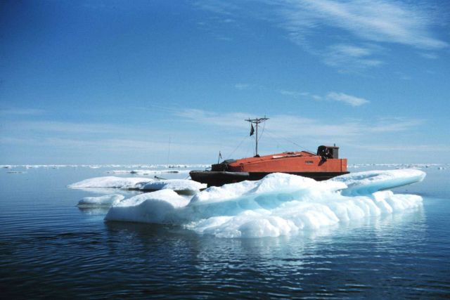 An orange boat accentuated by the blue water and bright white ice berg Picture