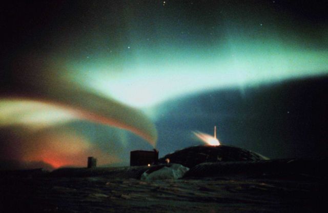 Aurora Australis - surrealistic view of South Pole station with auroral curtain and exhaust emanating in curved line fro Picture