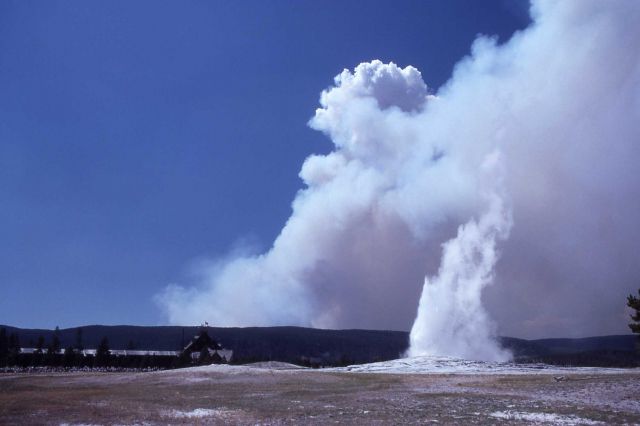 Old Faithful erupting & Old Faithful Inn with smoke plume in distance Picture