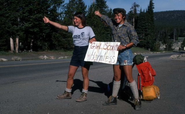 Two short-clad hitchhikers with a sign that reads 